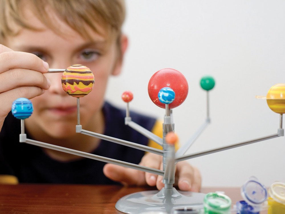 Child playing with a model of the solar system on a table.