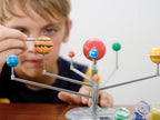 Child playing with a model of the solar system on a table.